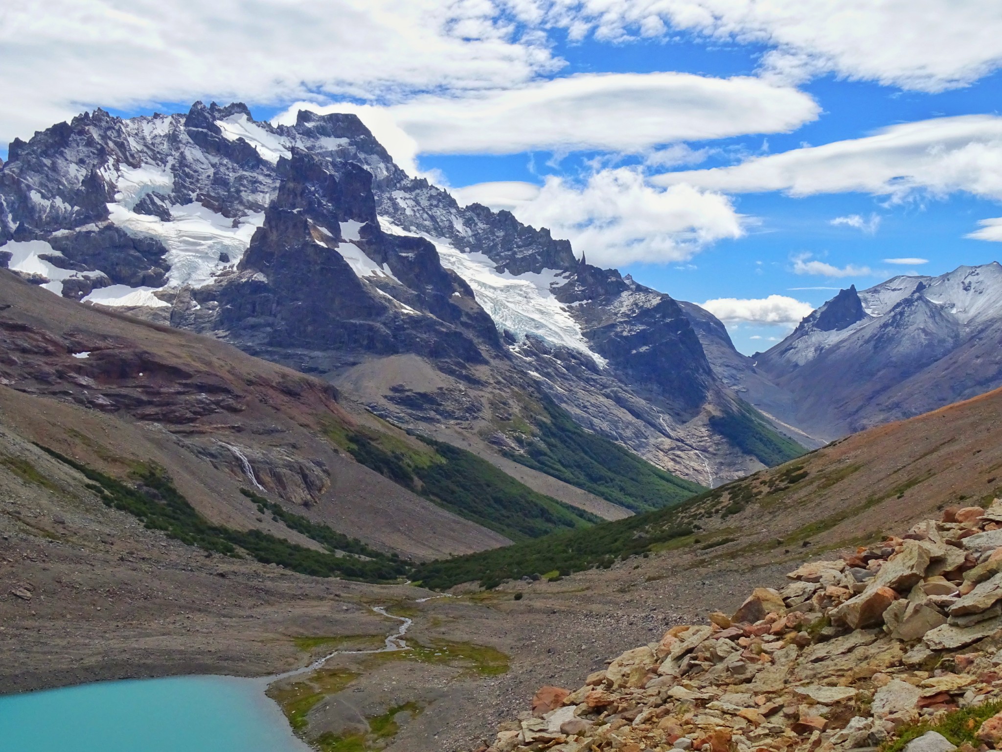 Mountain landscape in Patagonia with snow-capped peaks, glacial lake and valley under a blue sky.