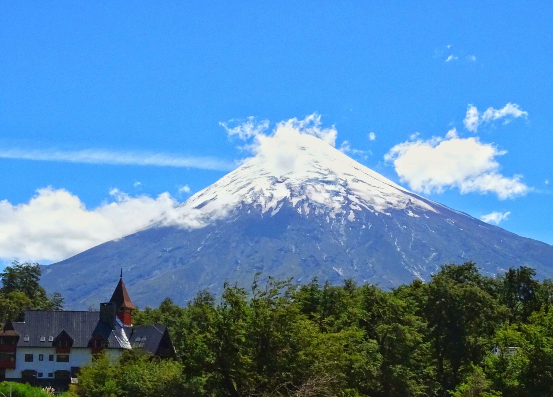 Snow-capped Osorno Volcano rising above forest and countryside beneath a bright blue sky.