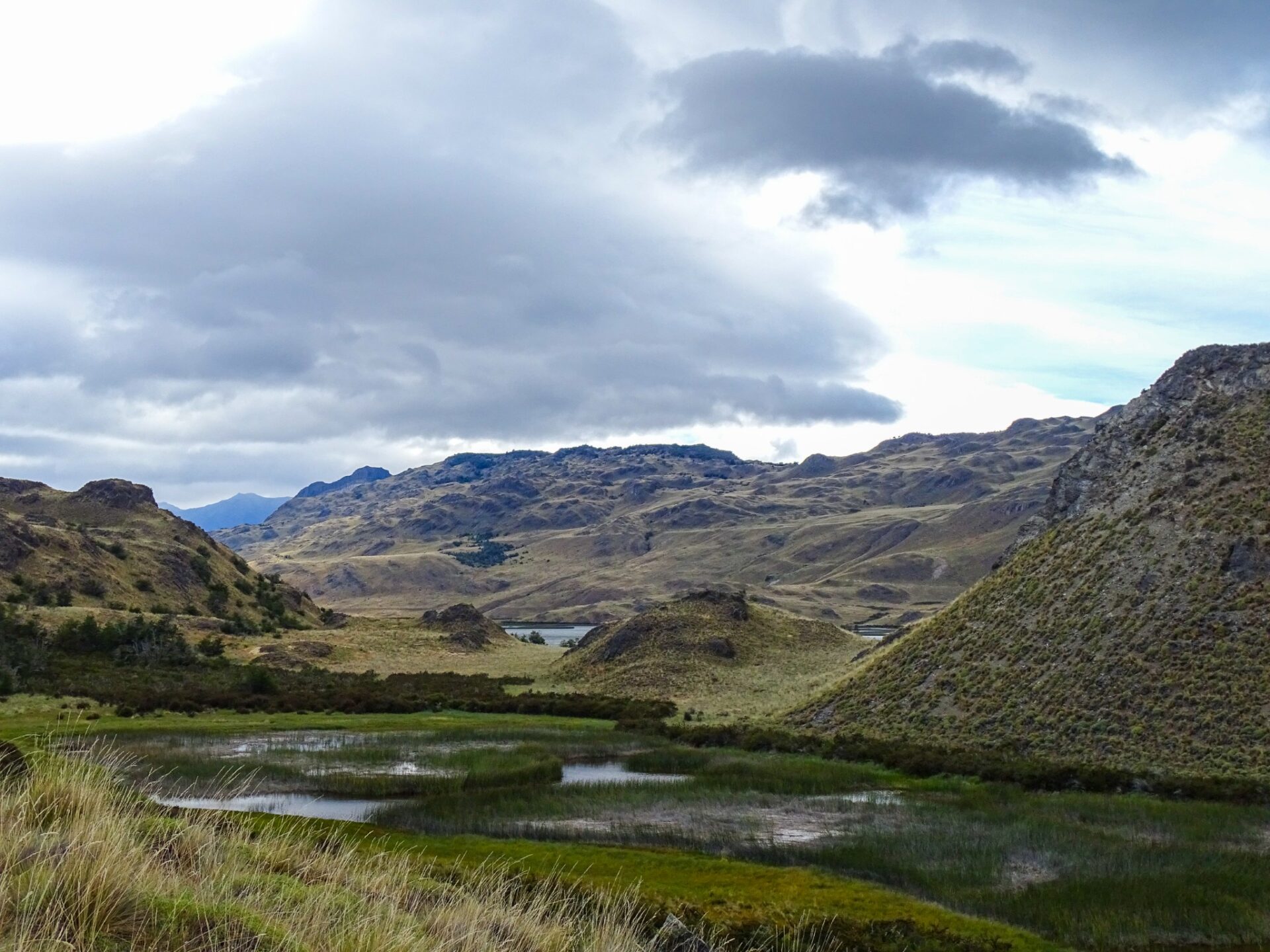 Rolling hills and wetlands in Patagonia National Park beneath dramatic cloud-filled skies.