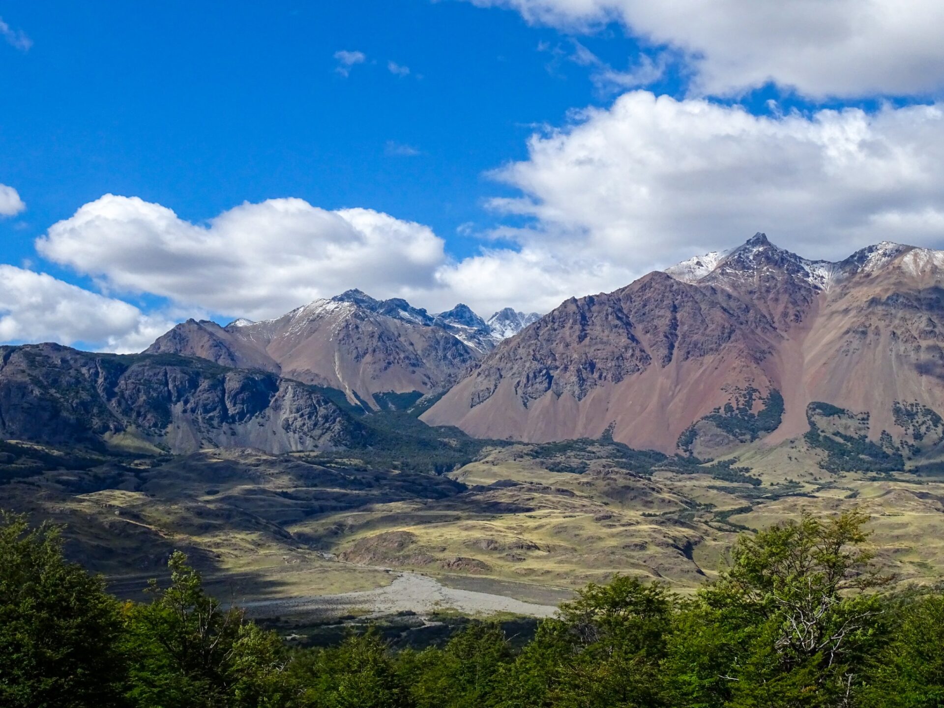 Patagonian landscape with river canyon, rolling hills, and dramatic storm clouds.