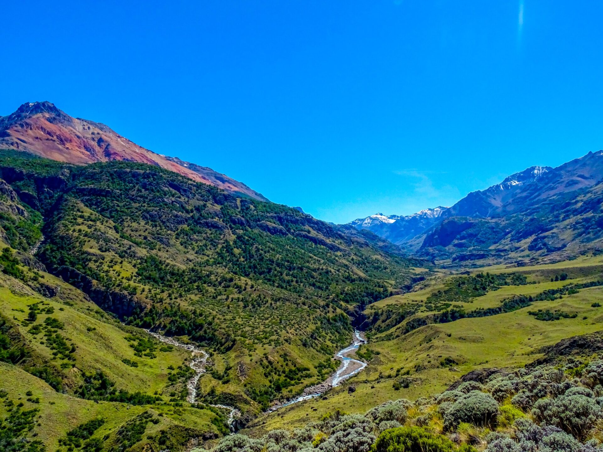 Mountain valley in Patagonia with winding river and snow-capped peaks under a clear blue sky.