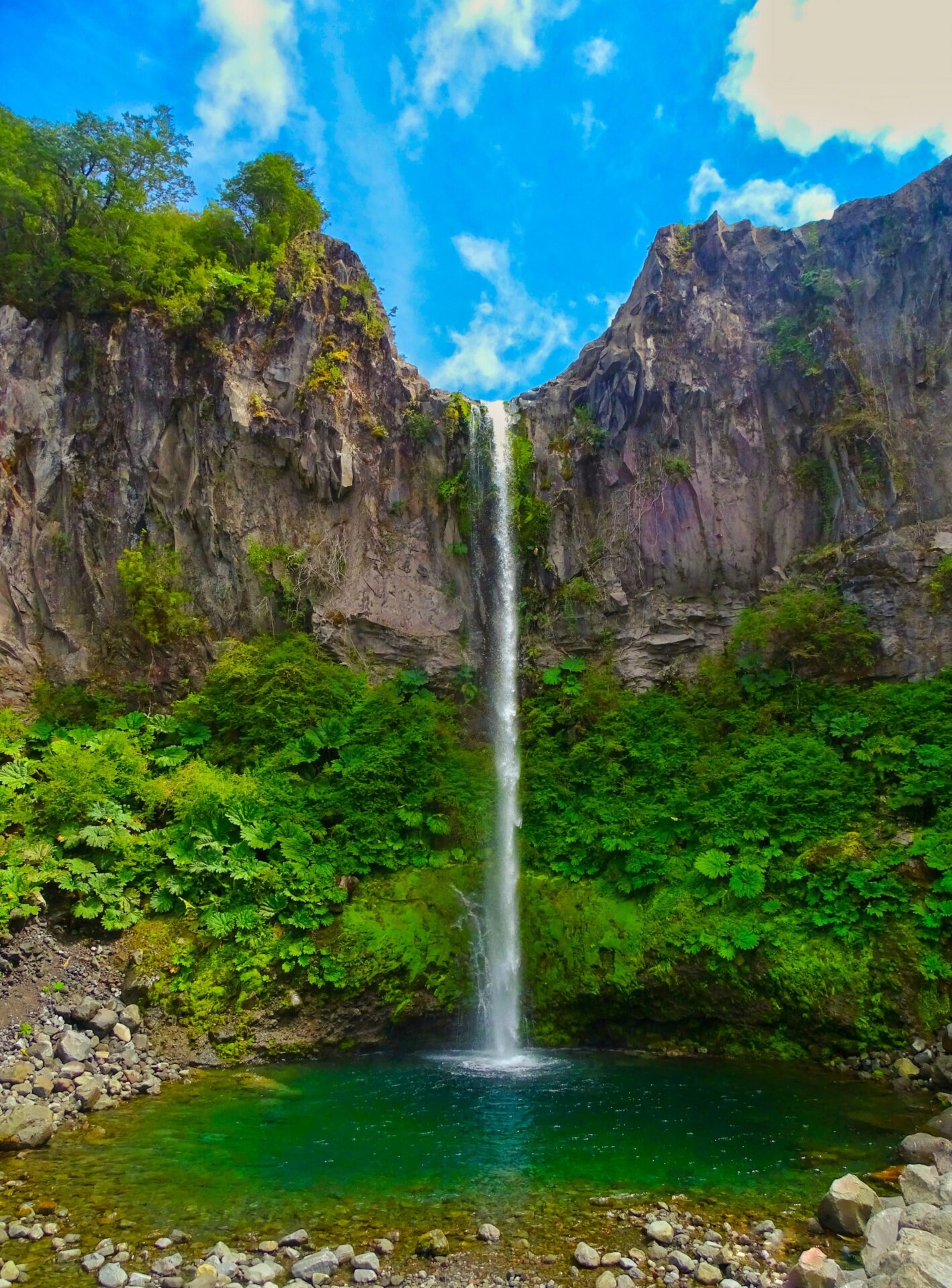 Salto Río Blanco waterfall cascading into an emerald pool surrounded by cliffs and lush vegetation.