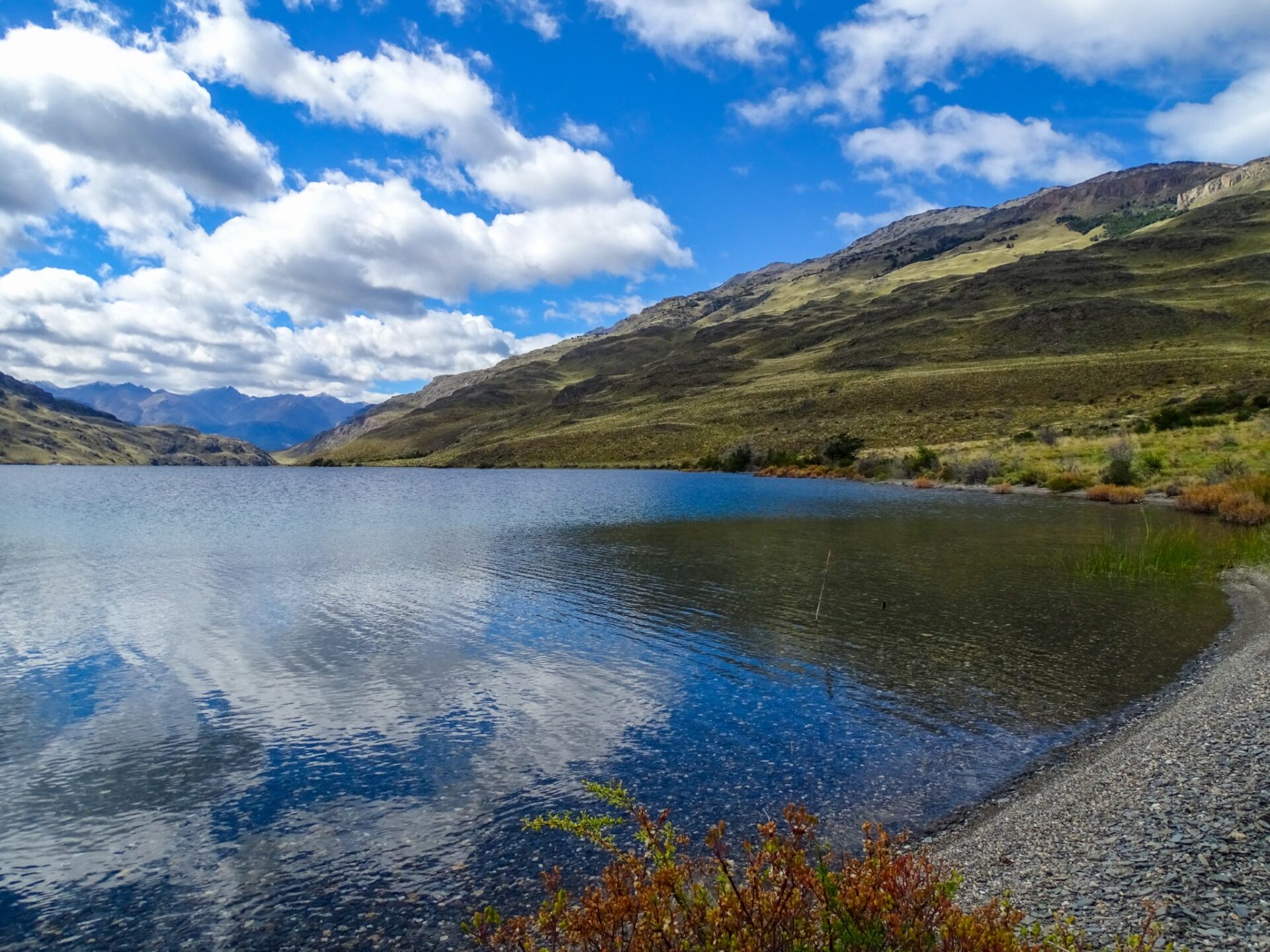 Lago Gutiérrez reflecting clouds and surrounding hills beneath a bright mountain sky.