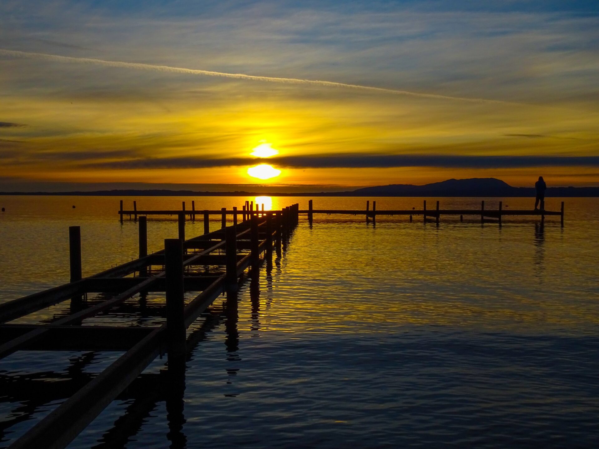 Sunset over Lago Villarrica with a wooden pier extending across calm waters.
