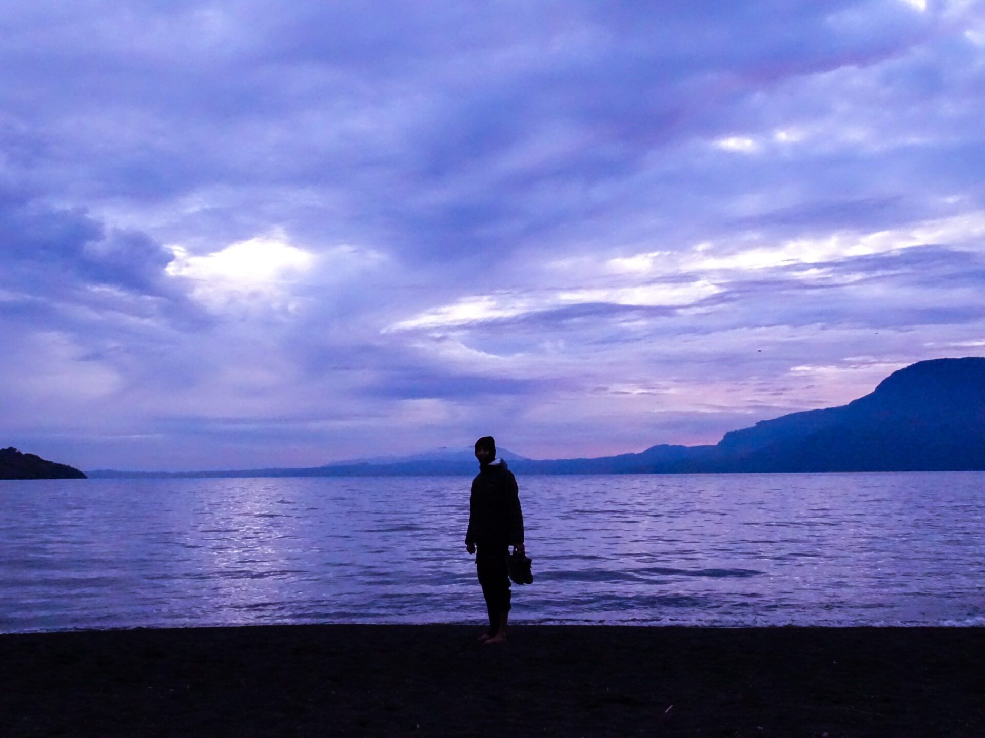 Person standing on the shore of Lago Villarrica beneath dramatic clouds at dusk.